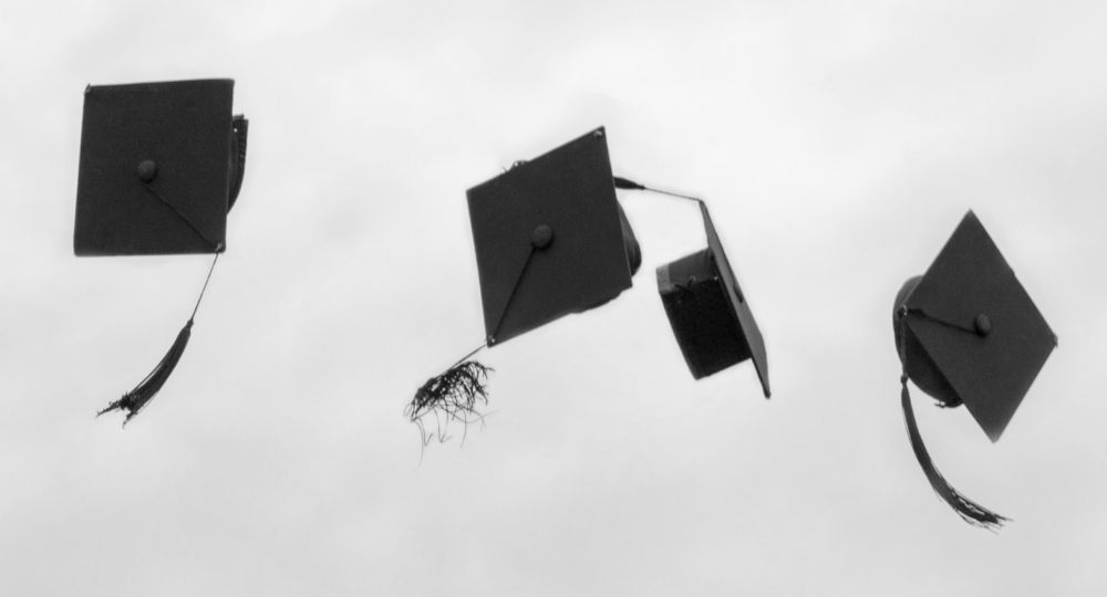 Graduation hats thrown up in the air against a grey cloudy day