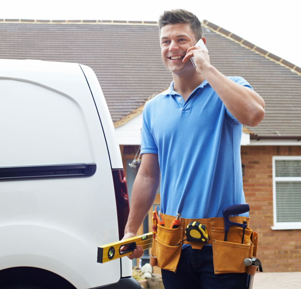 Builder carrying his tools answering the phone in front of a white van