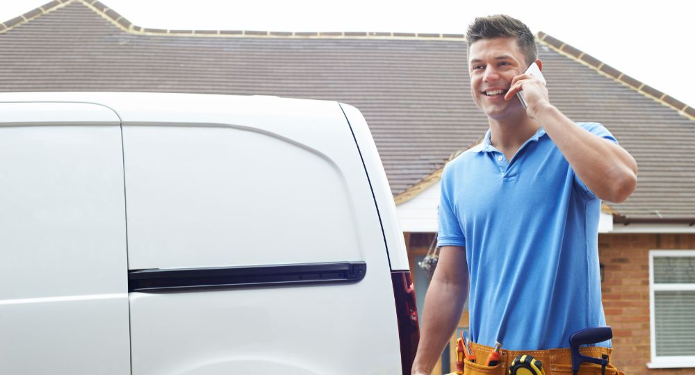 Builder carrying his tools answering the phone in front of a white van