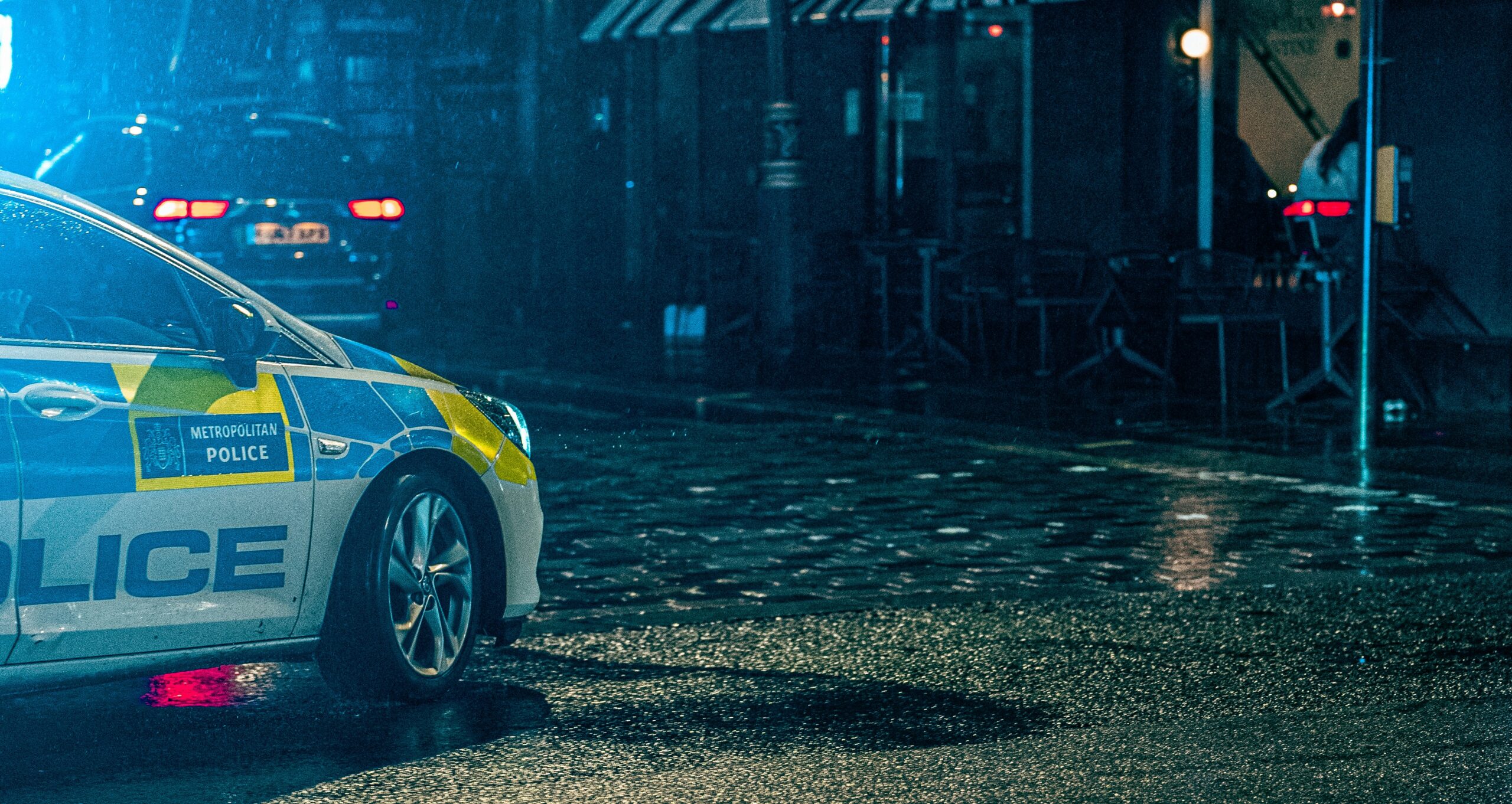 A police car is parked on a wet, cobblestone street at night.