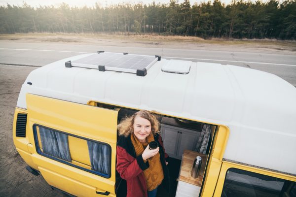 Young person looking out of camper van with solar panel on the roof top and pine forest on the background