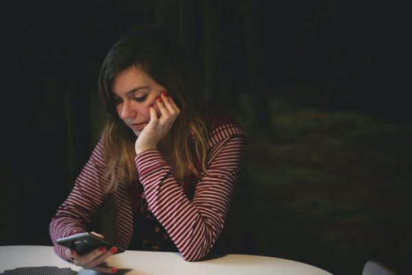 Woman sat at table, head resting on one hand, casually looking at phone