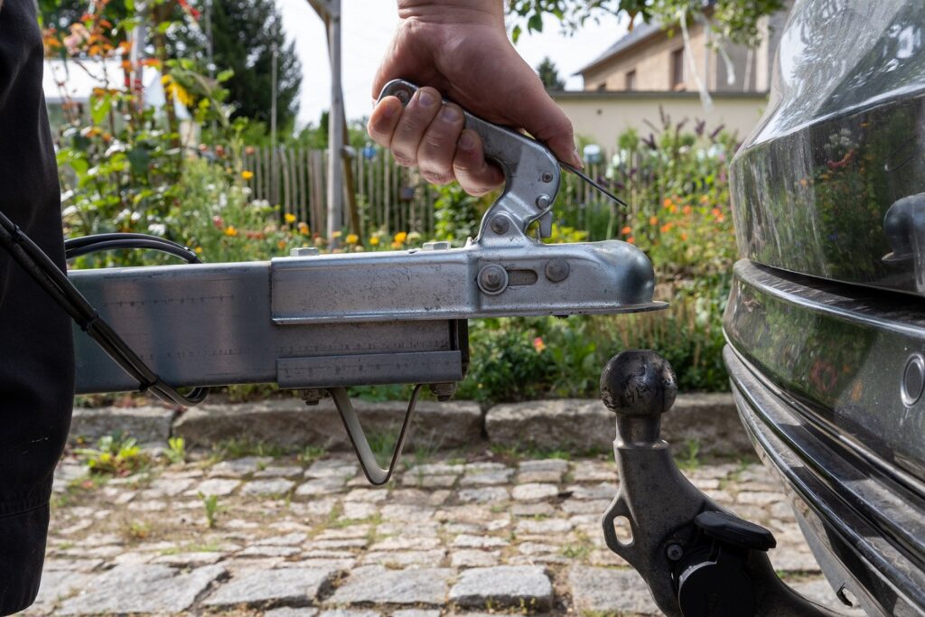 Man's hand checks the fixation of the trailer closed hitch lock handle on the towing ball towbar of the car