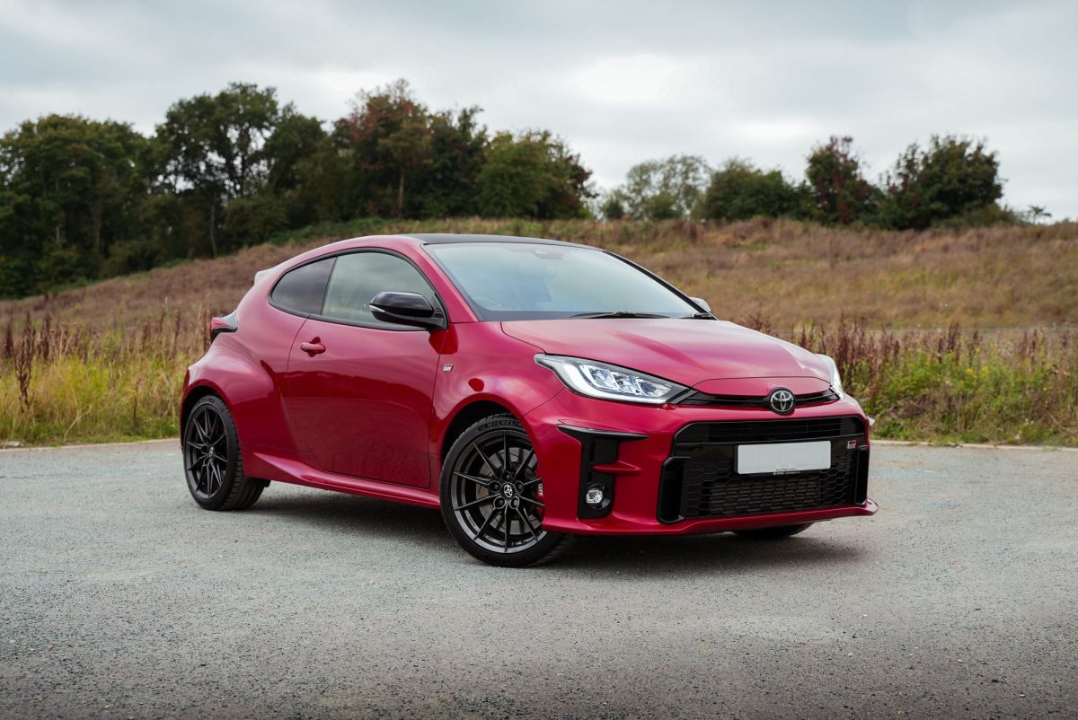 Toyota Yaris parked in front of a green field and trees